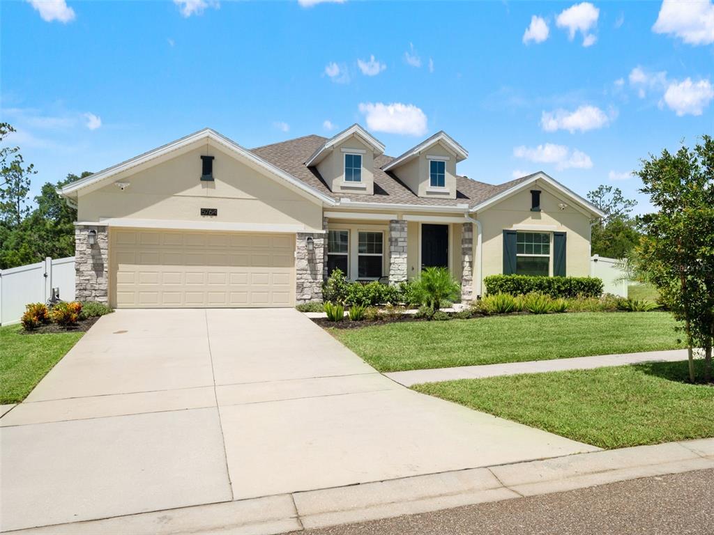 A single-story house with a beige stucco exterior, stone accents, and a two-car garage — 5764 ALENLON WAY, MOUNT DORA, FL
