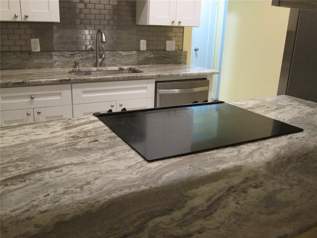 A kitchen features white cabinets, a gray tiled backsplash, and a large stone countertop island — 3925 W BAY VIEW AVENUE, TAMPA, FL