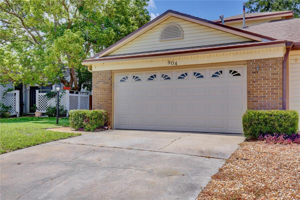 A beige garage door with windows is centered on the brick facade of a house — 904 NORFOLK COURT, LONGWOOD, FL