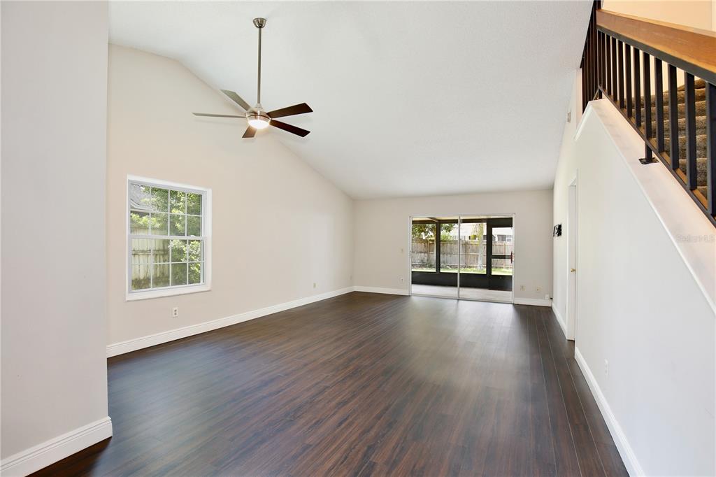 A spacious living room features dark wood flooring, a vaulted ceiling with a fan, and stairs — 904 NORFOLK COURT, LONGWOOD, FL