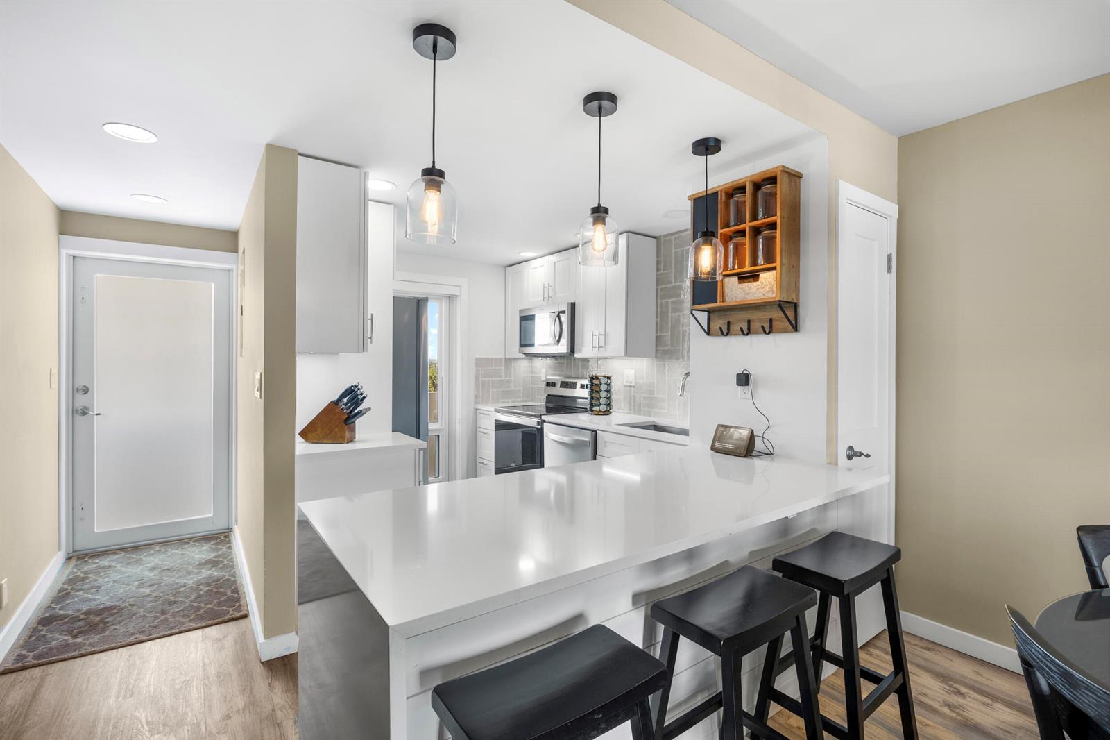 A kitchen with a white quartz breakfast bar, three black stools, and pendant lighting — 1630 N Ocean Boulevard # 812, Pompano Beach FL 33062, POMPANO BEACH, FL