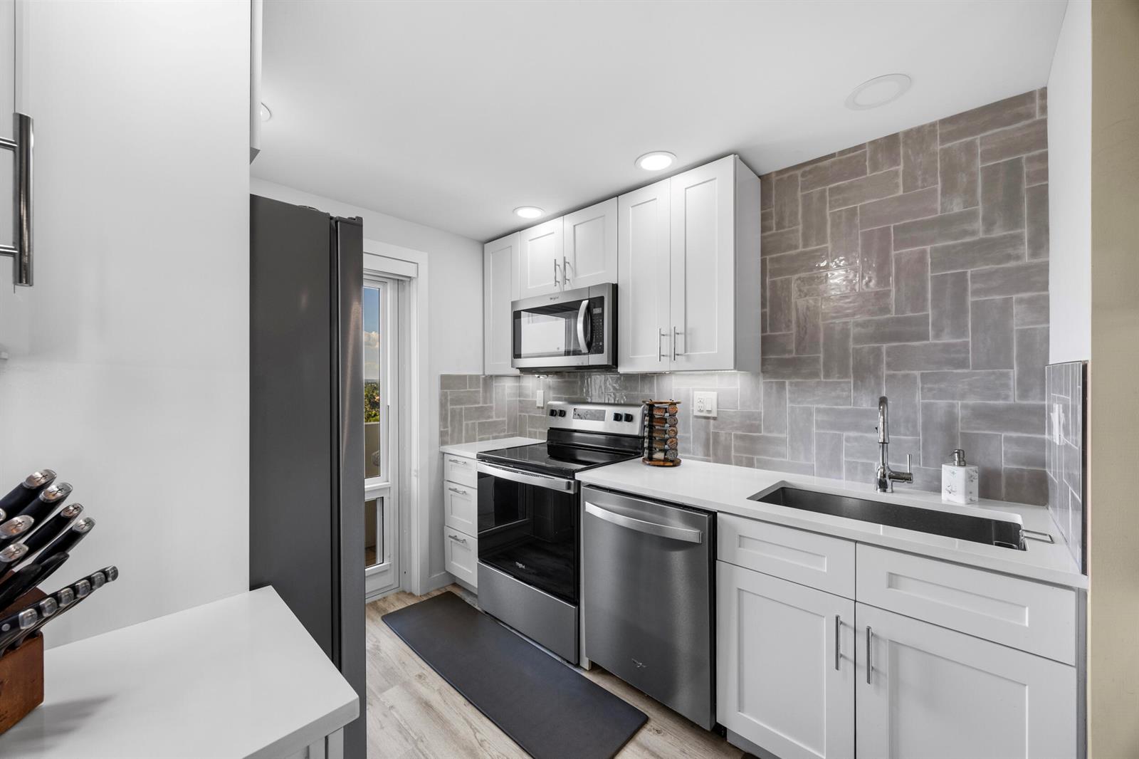 A modern kitchen features white cabinets, stainless steel appliances, and a gray herringbone tile backsplash — 1630 N Ocean Boulevard # 812, Pompano Beach FL 33062, POMPANO BEACH, FL
