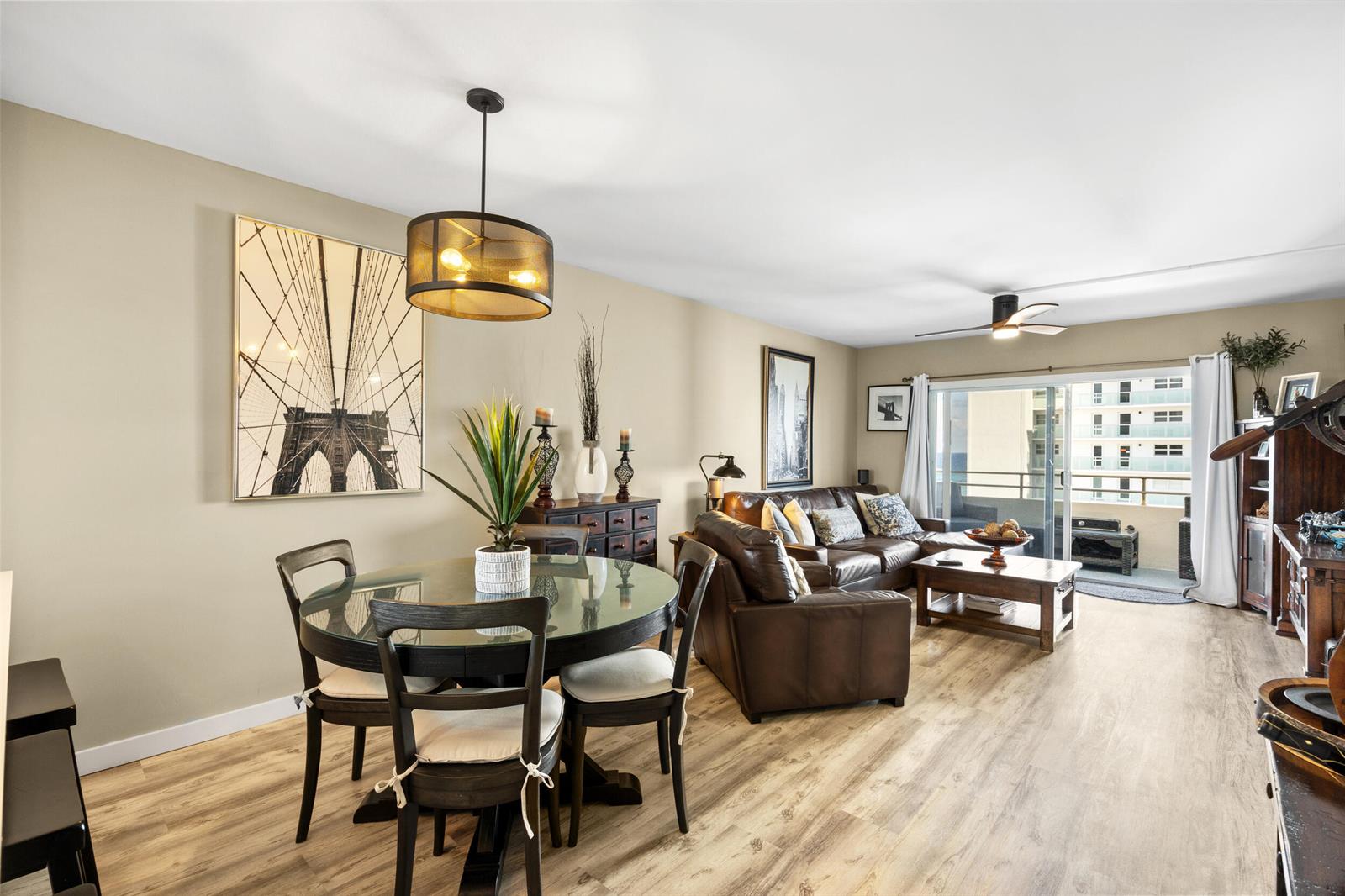A living and dining area with wood-look flooring, a glass-top table, and leather furniture — 1630 N Ocean Boulevard # 812, Pompano Beach FL 33062, POMPANO BEACH, FL