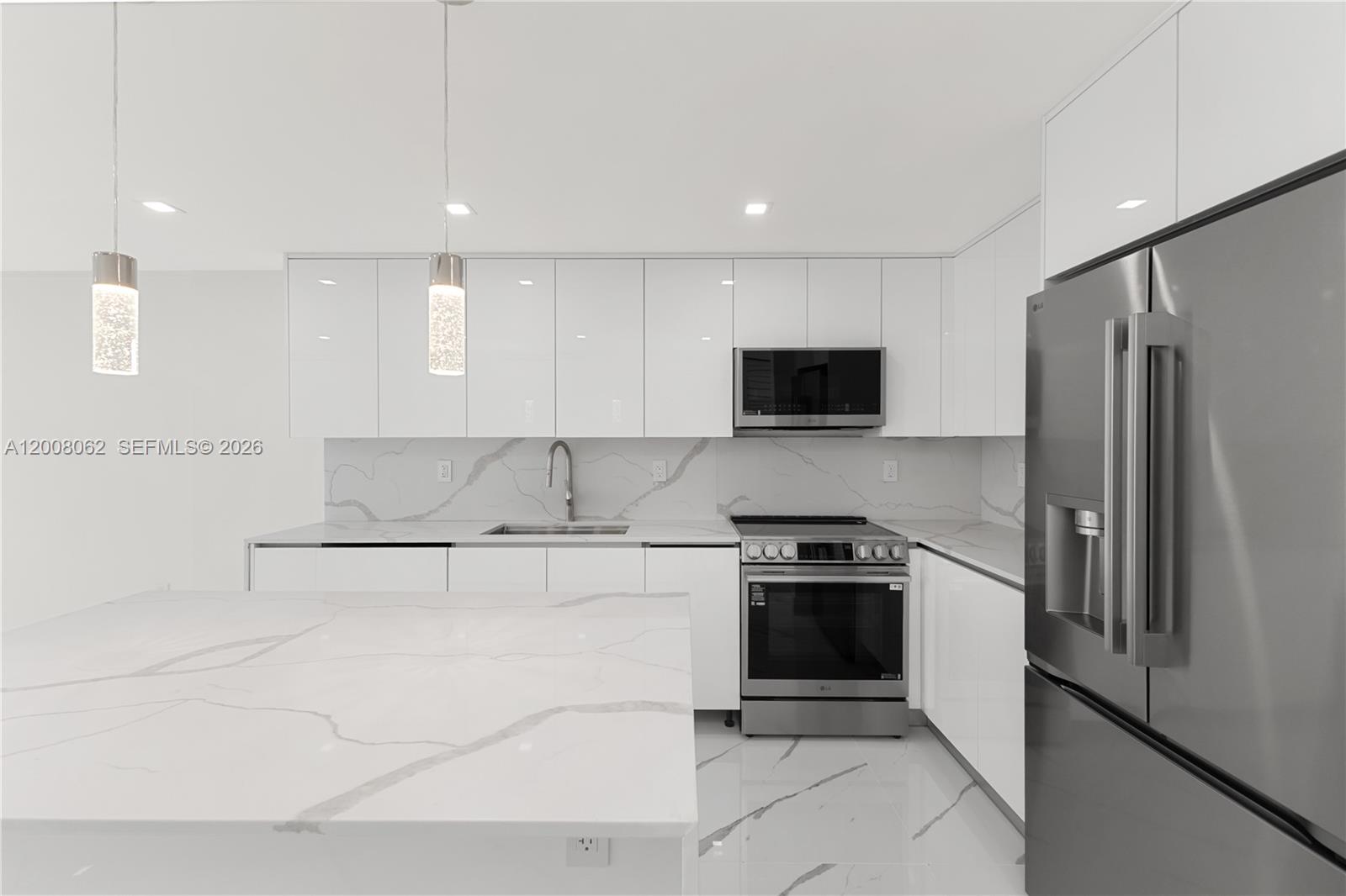 A modern kitchen features white glossy cabinets, marble-patterned countertops, and stainless steel appliances — 345 Ocean Dr # 708, Miami Beach FL 33139, MIAMI BEACH, FL