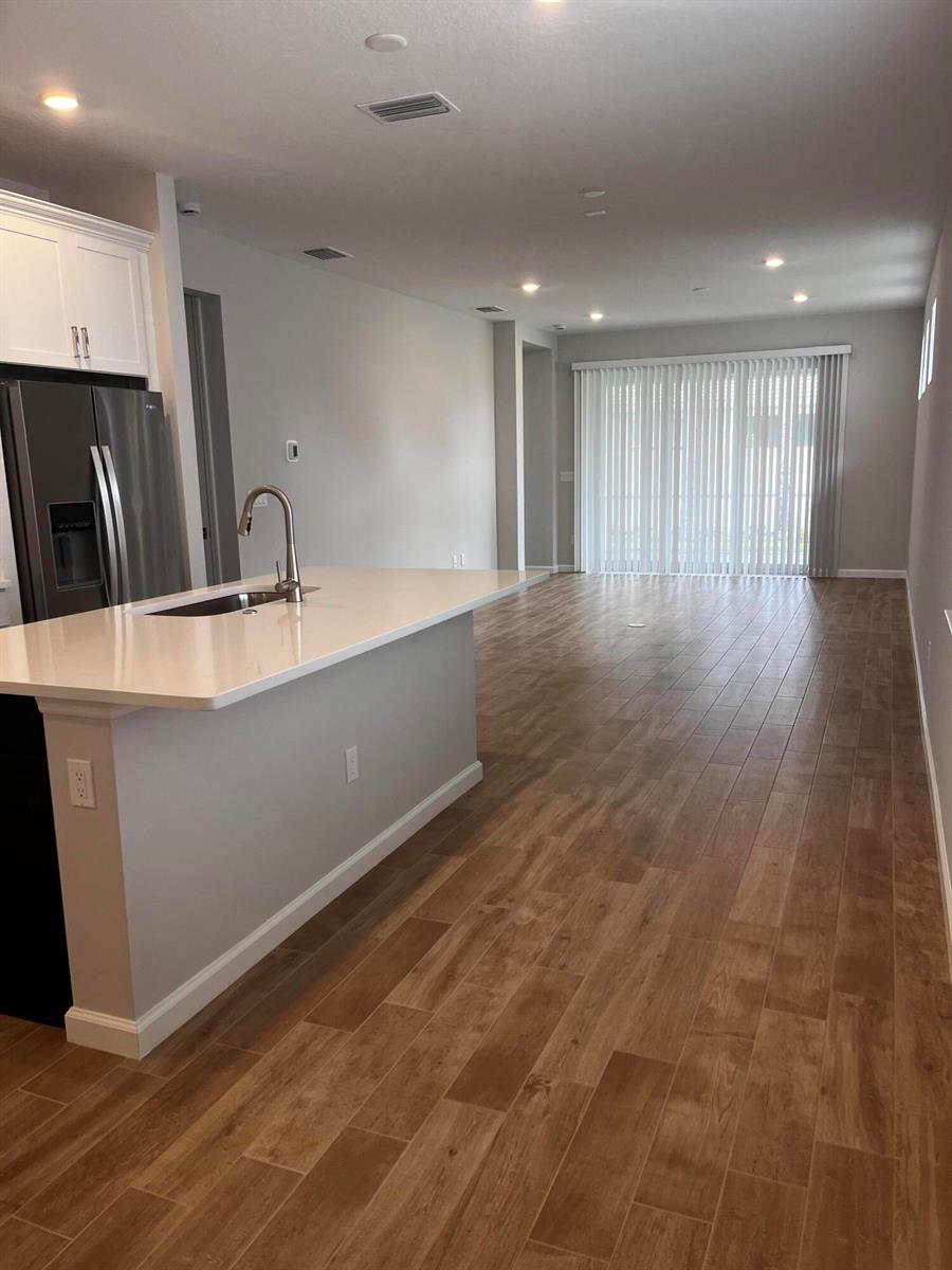A kitchen island with a sink faces an open living area with wood-look tile flooring — 4520 Jolly Roger Manor, Vero Beach FL 32967, VERO BEACH, FL