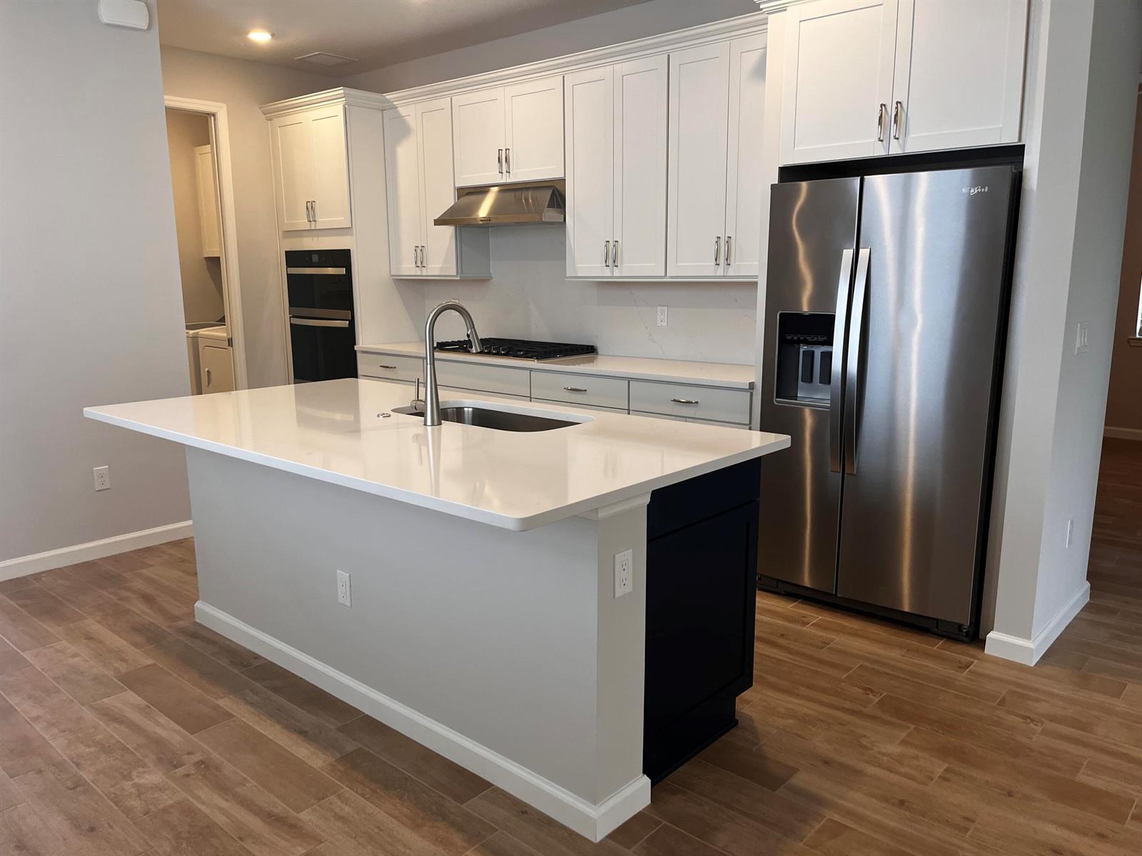 A modern kitchen features a white quartz island, stainless steel appliances, and white cabinetry — 4520 Jolly Roger Manor, Vero Beach FL 32967, VERO BEACH, FL