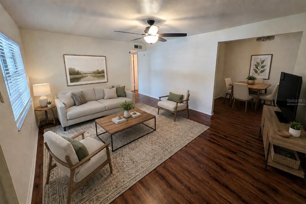 A living room with wood floors, a sofa, two armchairs, and an adjacent dining area — 700 E AIRPORT BOULEVARD UNIT H5, SANFORD, FL