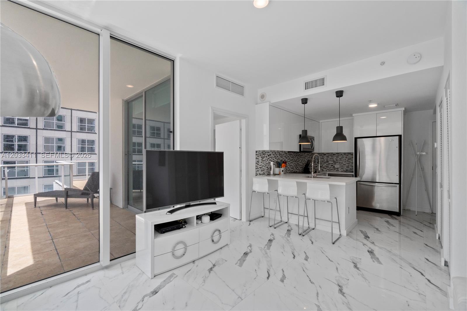 A modern kitchen and living area with white marble floors, a balcony, and breakfast seating — 300 S Biscayne Blvd # 1411, Miami FL 33131, MIAMI, FL
