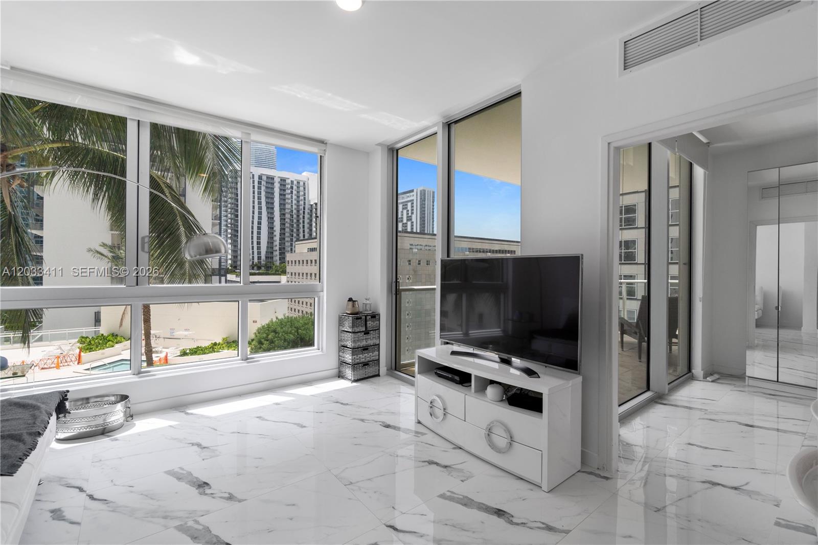 A bright living room features white marble floors, a television on a stand, and floor-to-ceiling windows — 300 S Biscayne Blvd # 1411, Miami FL 33131, MIAMI, FL