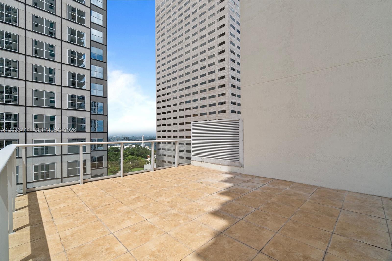A tiled balcony features a white metal railing overlooking a city view between two buildings — 300 S Biscayne Blvd # 1411, Miami FL 33131, MIAMI, FL