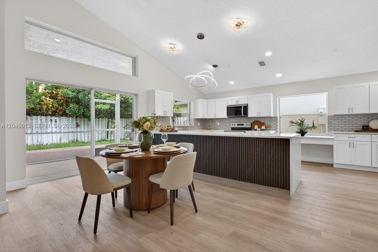 A modern kitchen features white cabinetry, a dark wood-slatted island, and an adjacent dining area — 116 W Bayridge Dr, Weston FL 33326, WESTON, FL