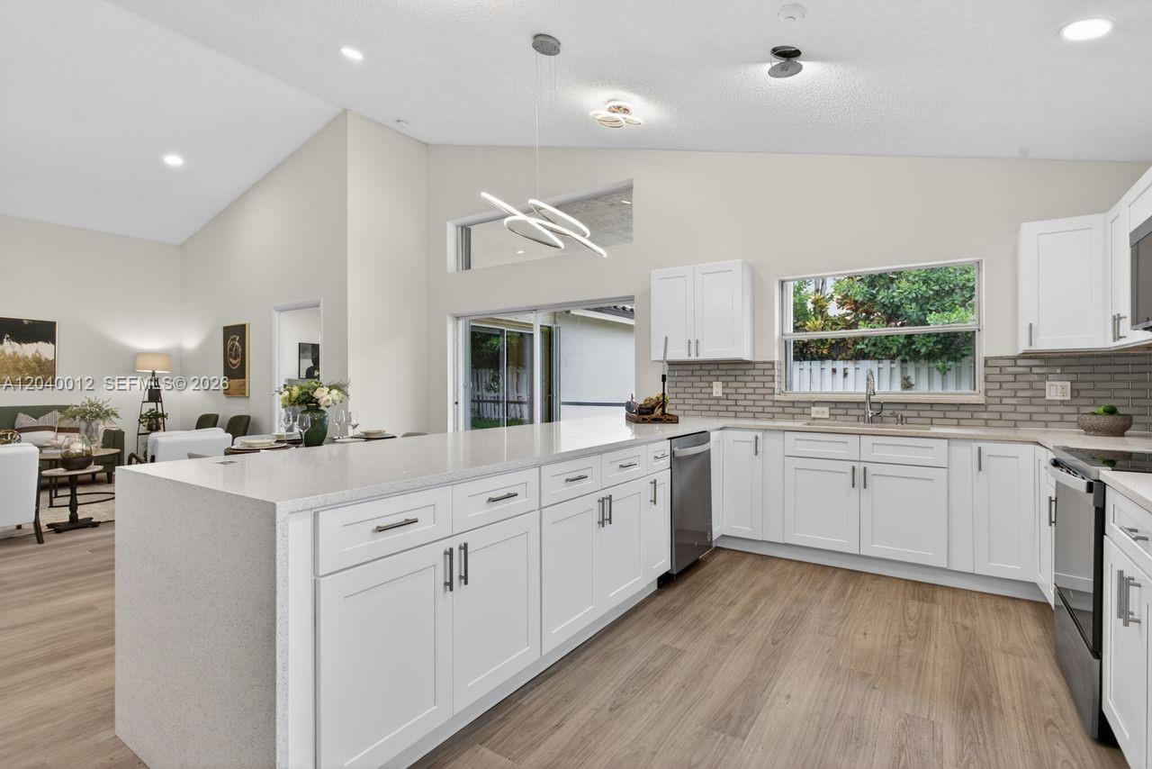 A modern kitchen features white cabinets, quartz countertops, a gray tile backsplash, and light wood flooring — 116 W Bayridge Dr, Weston FL 33326, WESTON, FL