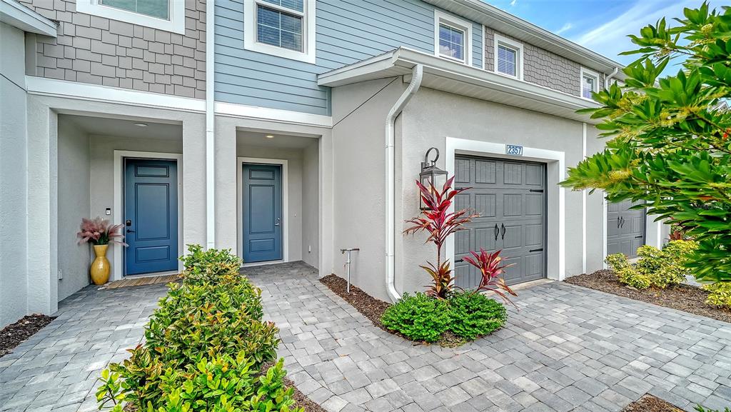 The exterior of a multi-unit townhouse features blue doors, gray garage doors, and paved walkways — 2357 WASHINGTON PALM COURT, BRADENTON, FL