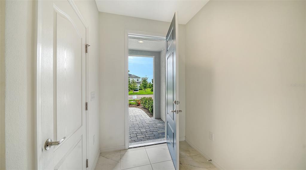 An open front door reveals a tiled entryway looking out onto a paved walkway and neighborhood — 2357 WASHINGTON PALM COURT, BRADENTON, FL