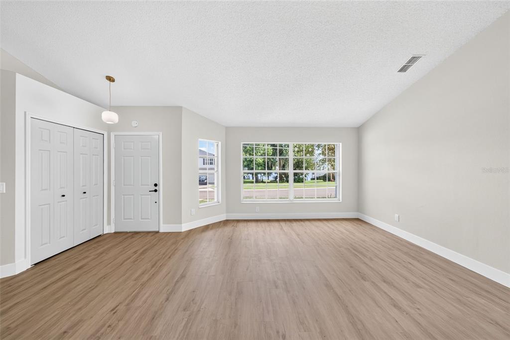 An empty living room features light wood-look flooring, white walls, and a large window — 294 LAKE DOE BOULEVARD, APOPKA, FL