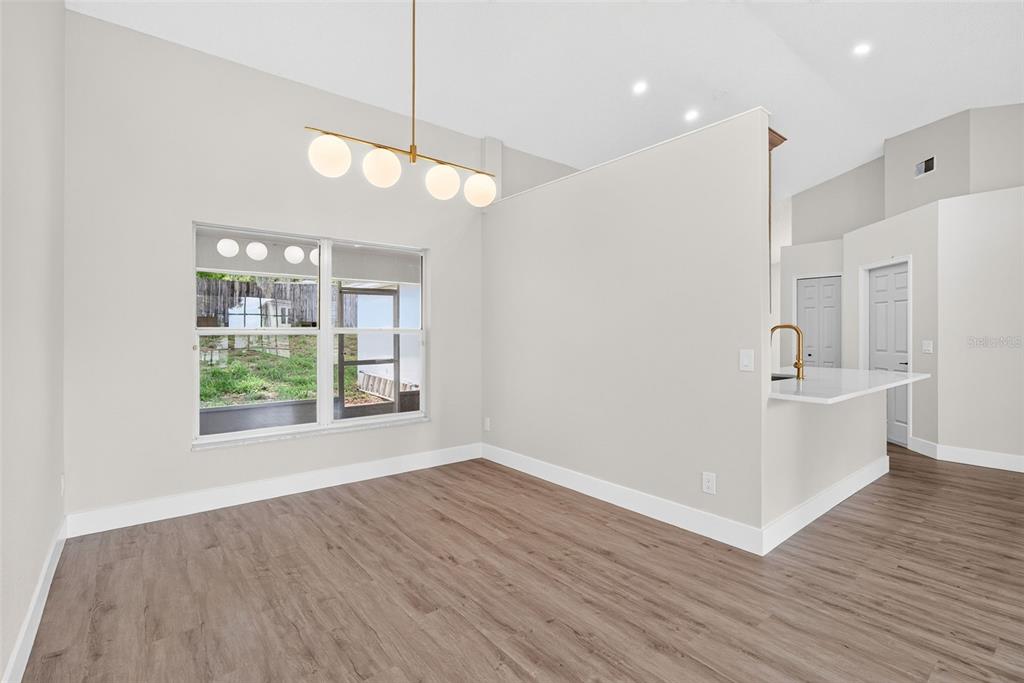 An empty dining area features wood-look flooring, a modern light fixture, and a kitchen pass-through — 294 LAKE DOE BOULEVARD, APOPKA, FL