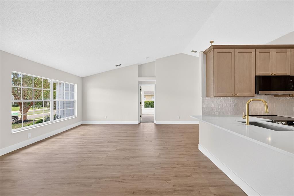 A bright living area with wood-look flooring, vaulted ceilings, and an adjacent kitchen with white countertops — 294 LAKE DOE BOULEVARD, APOPKA, FL