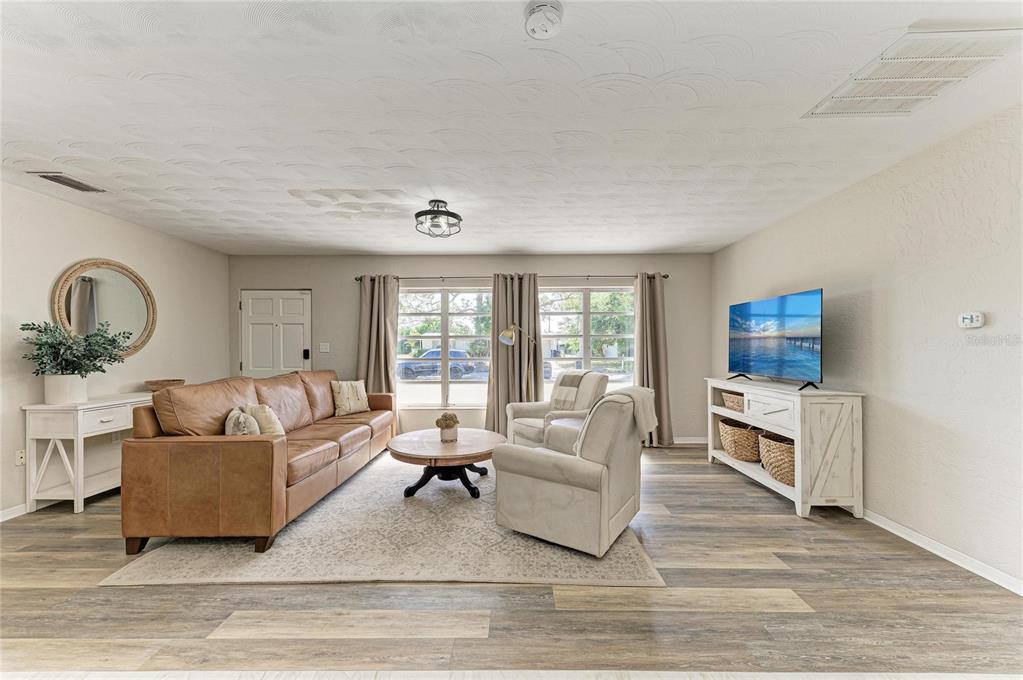 An open-concept living room and kitchen feature blue cabinets, leather seating, and wood-look flooring — 120 60TH STREET W, BRADENTON, FL
