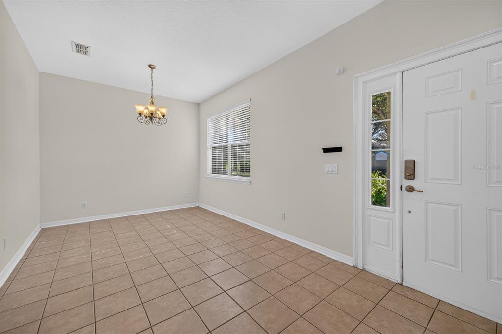 A dining room with beige tile flooring, a chandelier, and a white front door — 7516 BENTONSHIRE AVENUE, WINDERMERE, FL