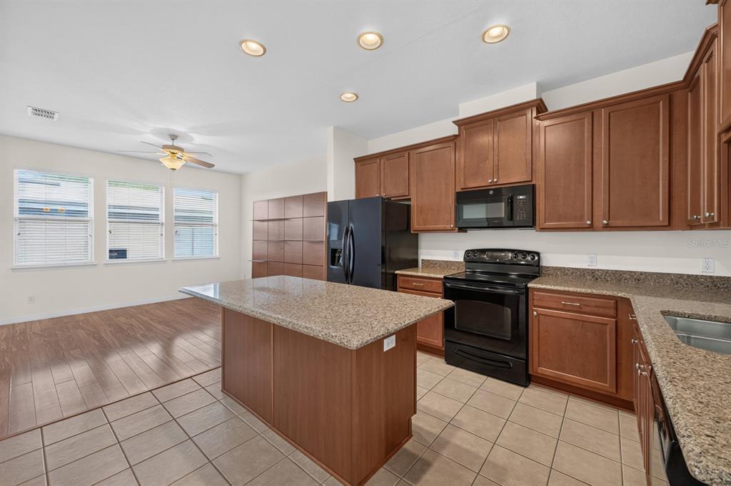 A kitchen with wood cabinets, granite countertops, black appliances, and a central island — 7516 BENTONSHIRE AVENUE, WINDERMERE, FL
