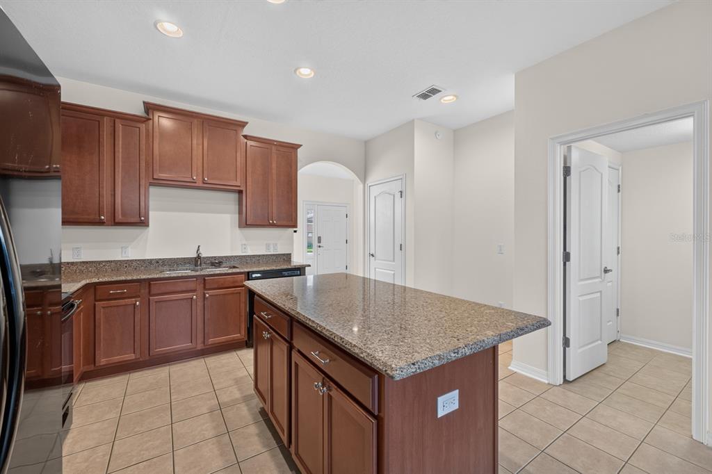 A kitchen features brown wooden cabinets, granite countertops, a central island, and tile flooring — 7516 BENTONSHIRE AVENUE, WINDERMERE, FL