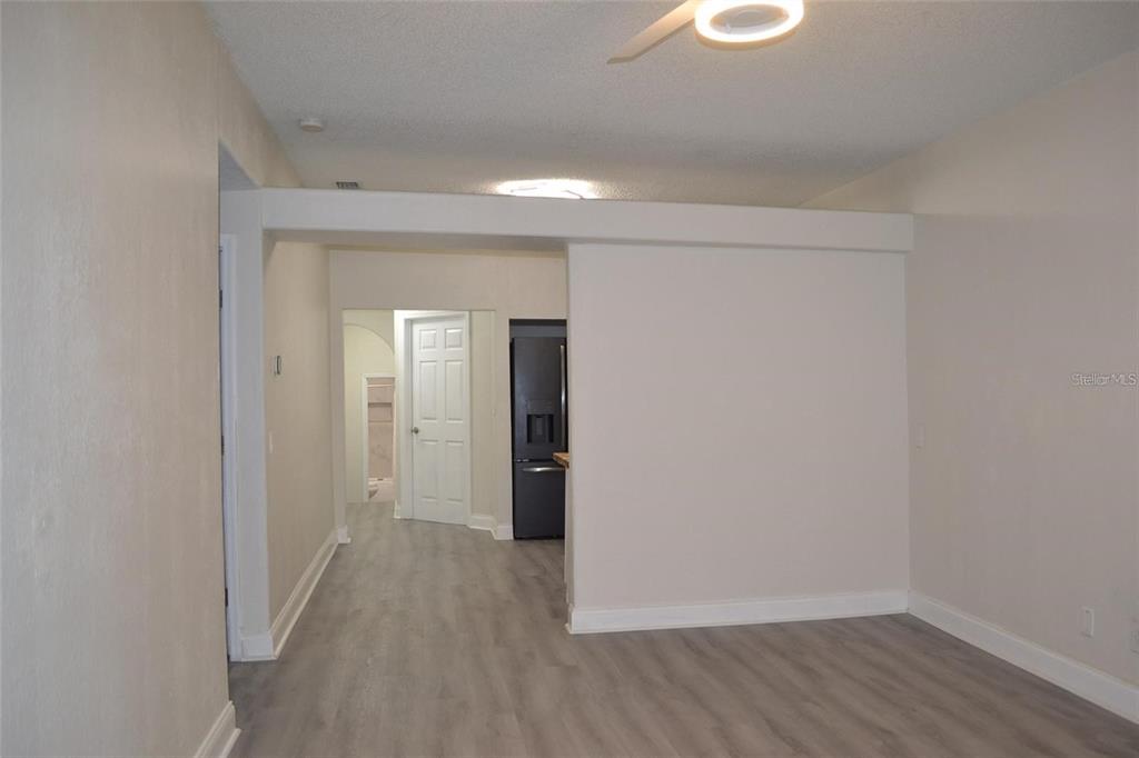 A view of a room with light wood-look flooring, a ceiling fan, and a kitchen doorway — 8210 N KLONDYKE STREET, TAMPA, FL