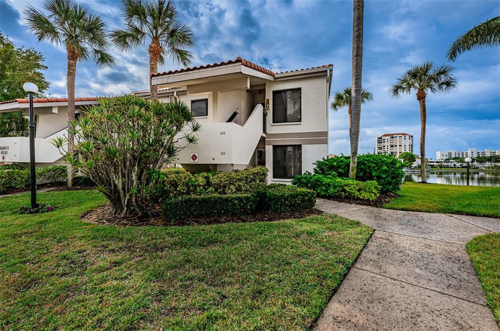 A two-story residential building with a concrete walkway, palm trees, and a nearby lake — 6281 BAHIA DEL MAR BOULEVARD UNIT 208, ST PETERSBURG, FL