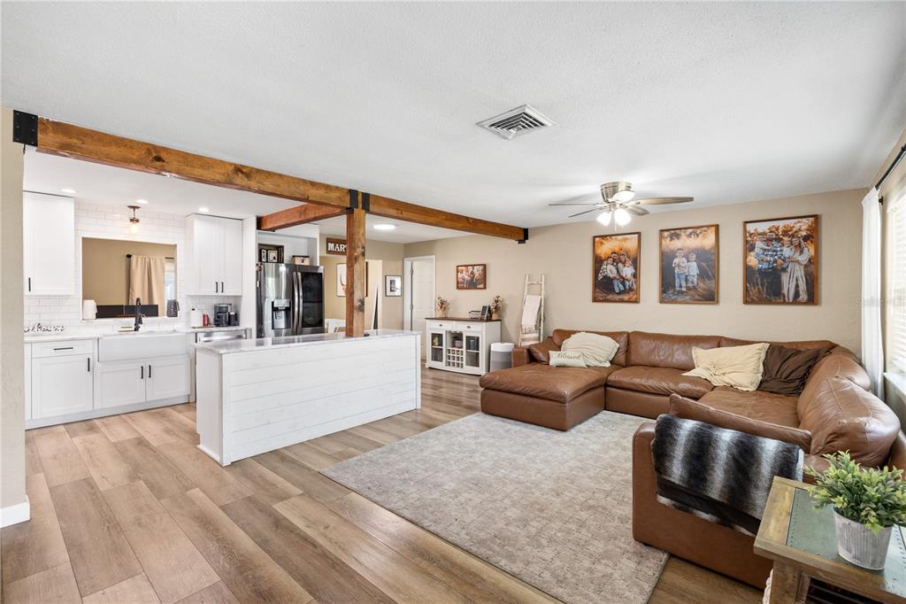 An open-concept living room and kitchen feature wood-look flooring, a leather sectional, and exposed beams — 6623 12TH TERRACE N, ST PETERSBURG, FL