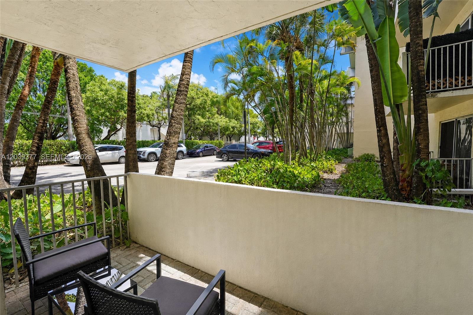A ground-level patio with two chairs overlooks a parking lot and tropical landscaping — 8950 SW 69th Ct # 109, Pinecrest FL 33156, PINECREST, FL
