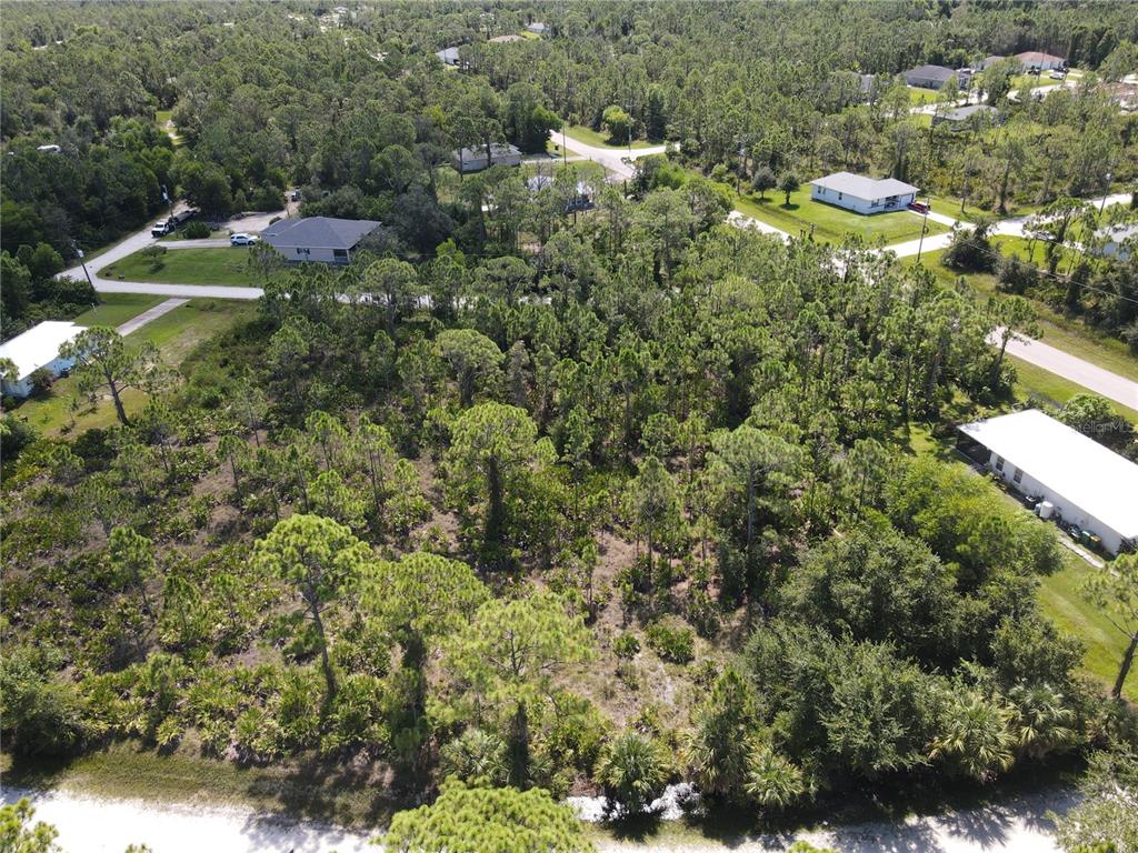 An aerial view shows a wooded, undeveloped residential lot surrounded by houses and paved roads — 12260 ESCUELA DRIVE, PUNTA GORDA, FL