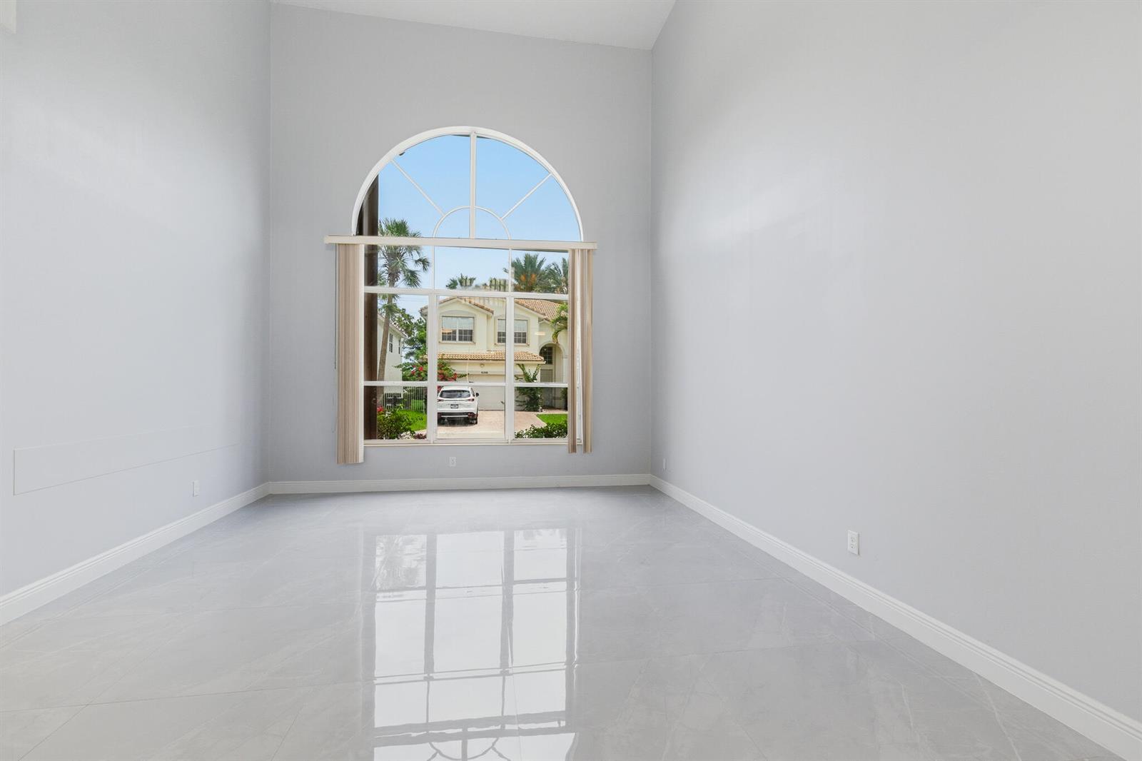 An empty room with light gray walls, glossy tile flooring, and a large arched window — 12197 Colony Preserve Drive, Boynton Beach FL 33436, BOYNTON BEACH, FL