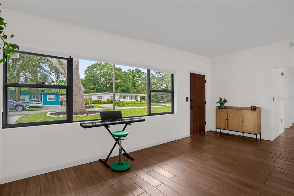 A living room with wood-look tile floors, a large window, a keyboard, and a wooden cabinet — 125 E LAUREN COURT, FERN PARK, FL