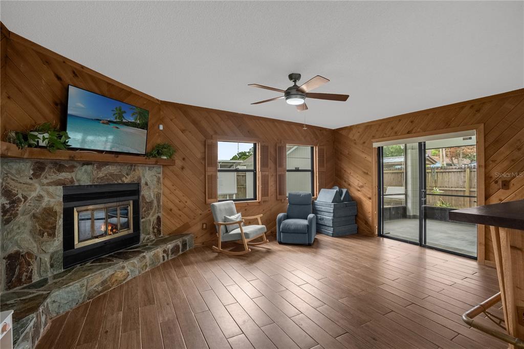 A living room features wood-paneled walls, a stone fireplace, tile flooring, and a ceiling fan — 125 E LAUREN COURT, FERN PARK, FL