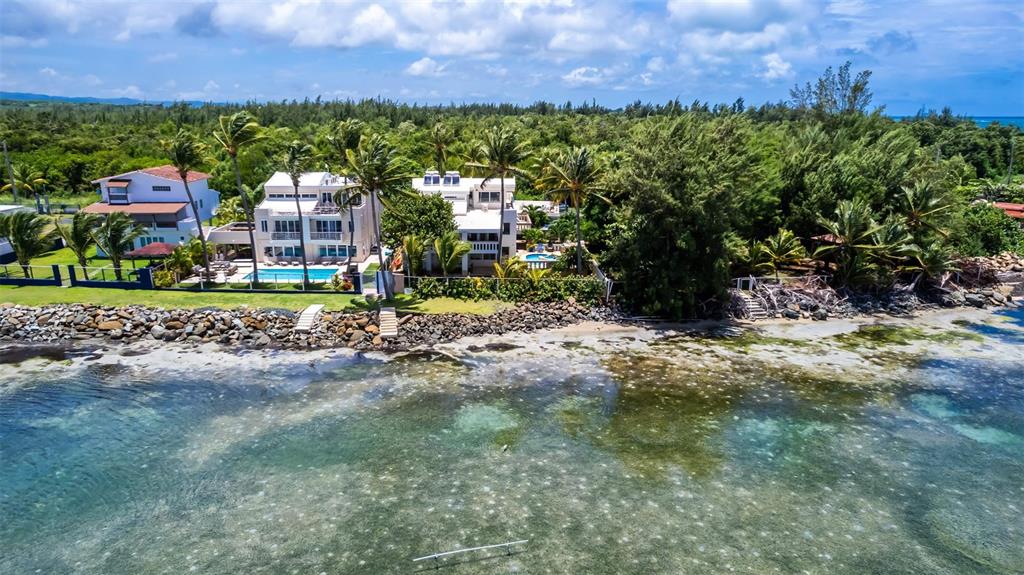An aerial view shows three beachfront houses with swimming pools along a rocky shoreline — Lot G Km 2.1 Carr. 968 LAS PICUAS, RIO GRANDE, PR