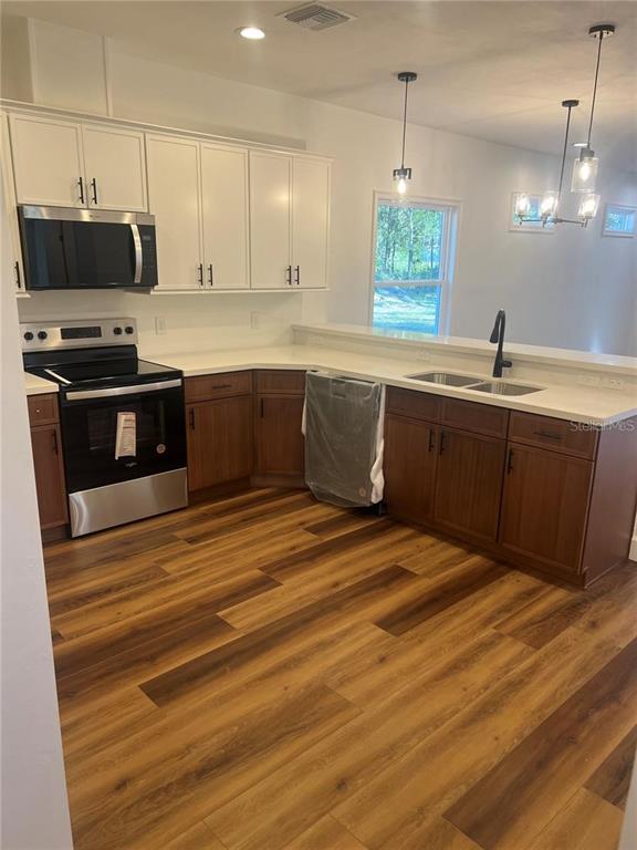 A kitchen features white upper cabinets, wood lower cabinets, stainless steel appliances, and wood flooring — 7848 SE 70TH AVENUE, TRENTON, FL