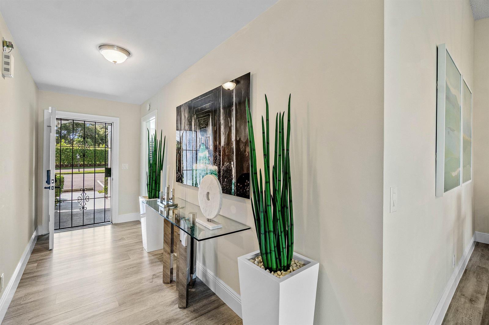 A bright entryway features a glass console table, tall potted plants, and a front door — 732 Lago Road, Delray Beach FL 33445, DELRAY BEACH, FL