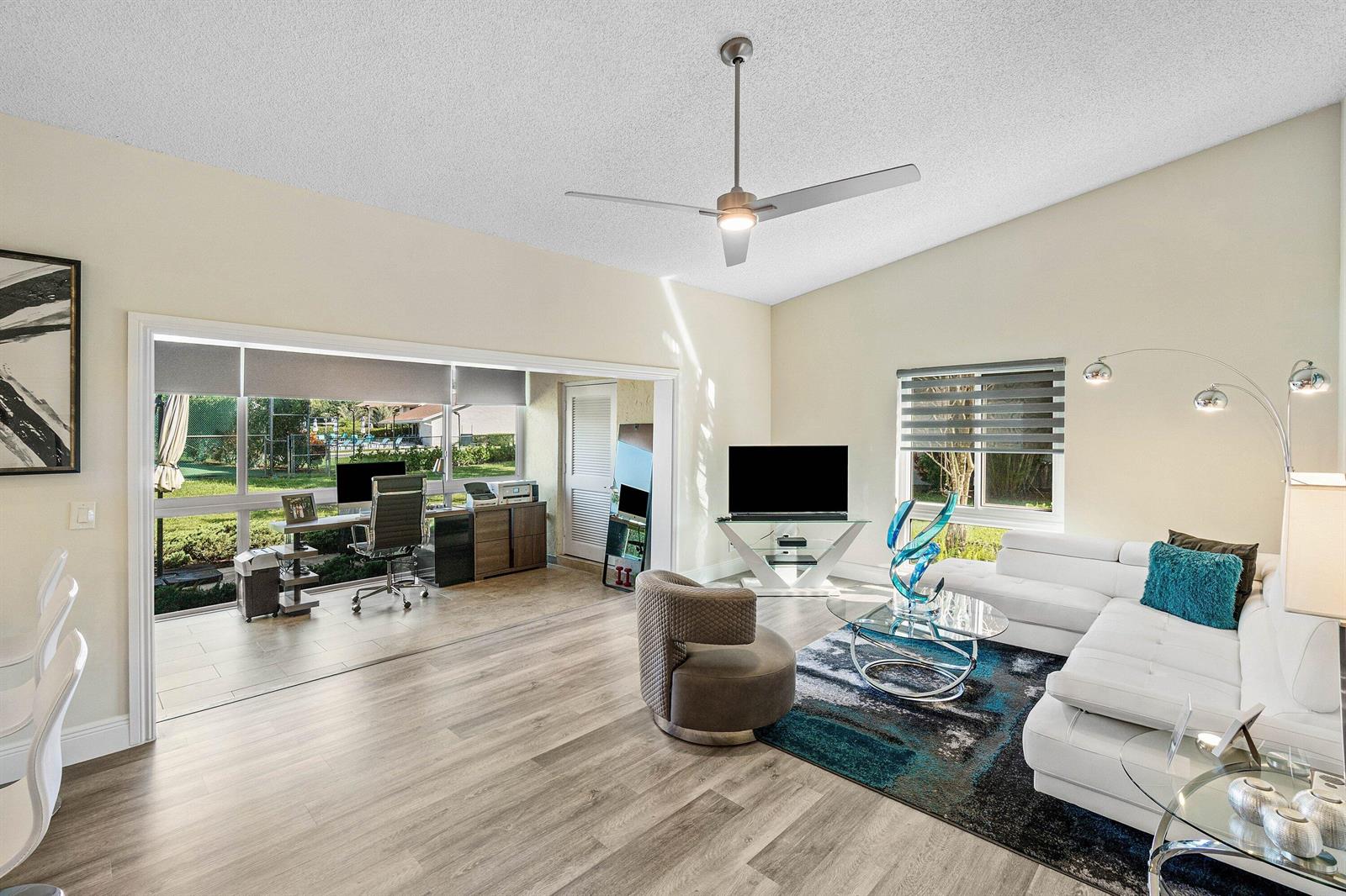 A living room with wood-look flooring, a white sectional, and a home office on the patio — 732 Lago Road, Delray Beach FL 33445, DELRAY BEACH, FL