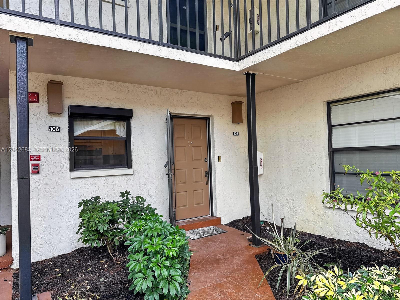 The exterior of a ground-floor apartment unit features a brown door and two windows — NAPLES, FL