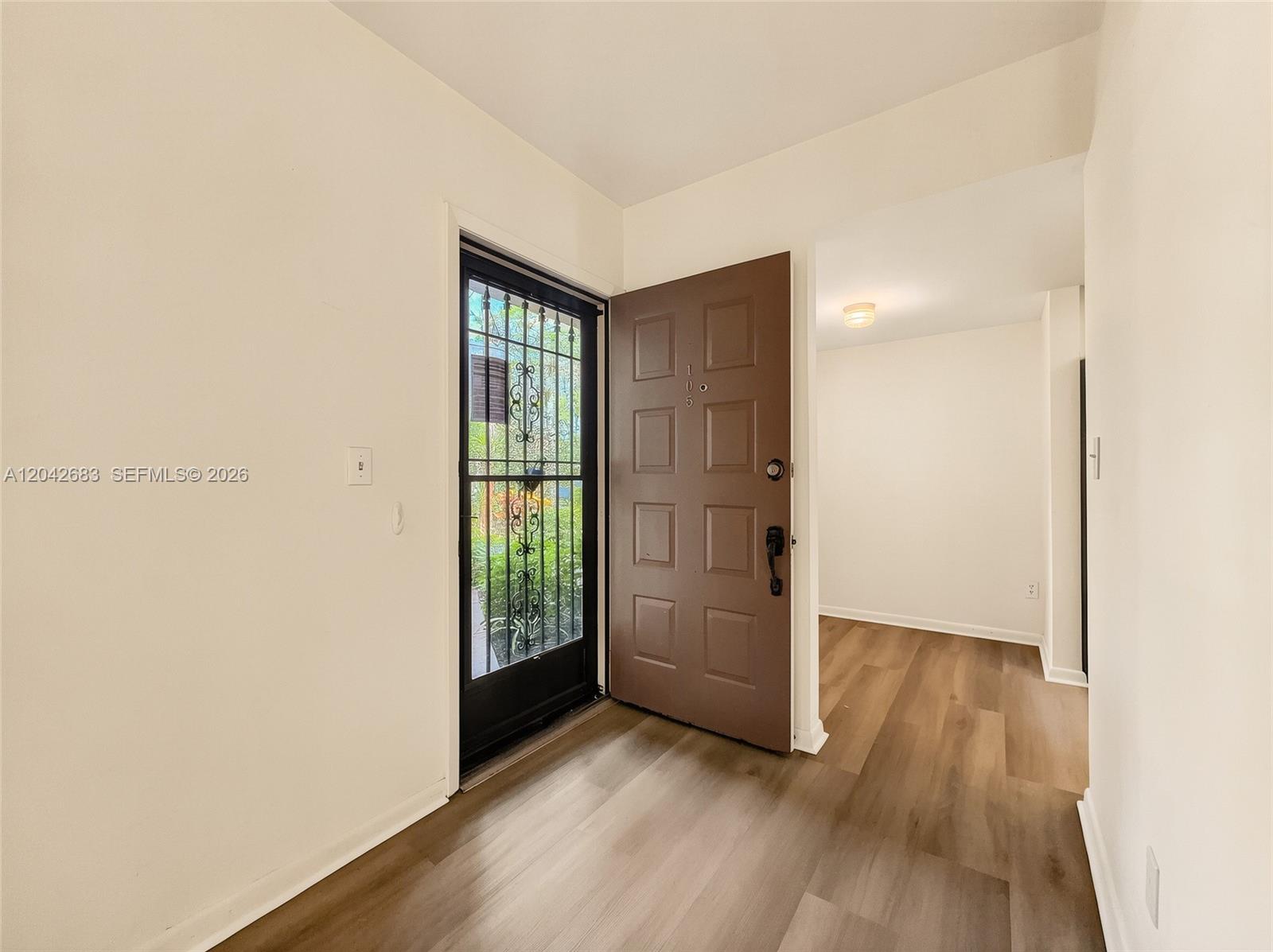 An entryway features wood-look flooring, a brown front door, and a black security screen door — NAPLES, FL