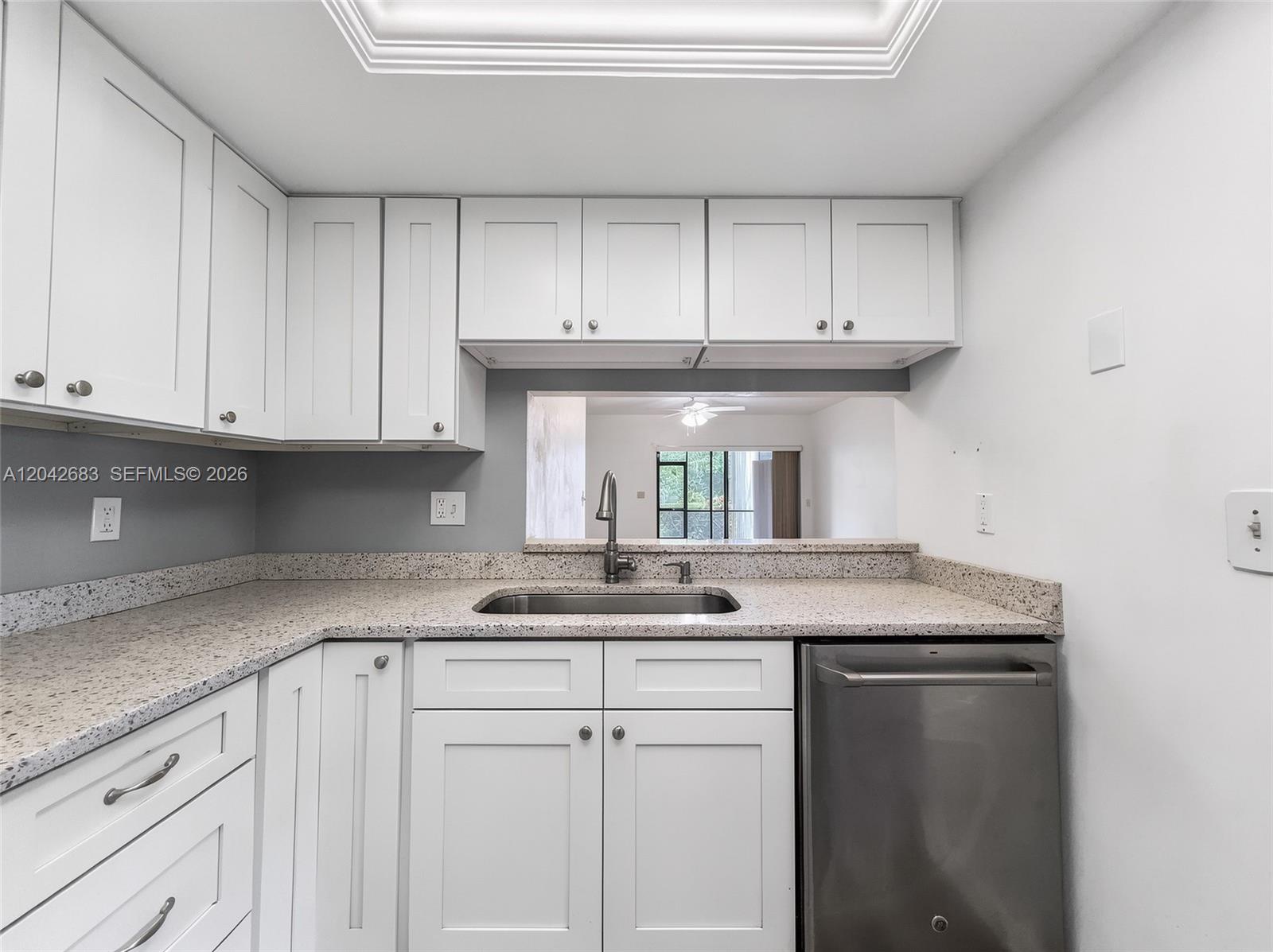 A kitchen features white cabinets, speckled granite countertops, a stainless steel sink, and a dishwasher — NAPLES, FL