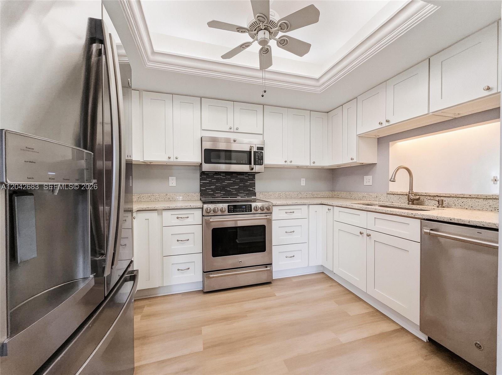 A kitchen features white cabinets, stainless steel appliances, light countertops, and a ceiling fan — NAPLES, FL