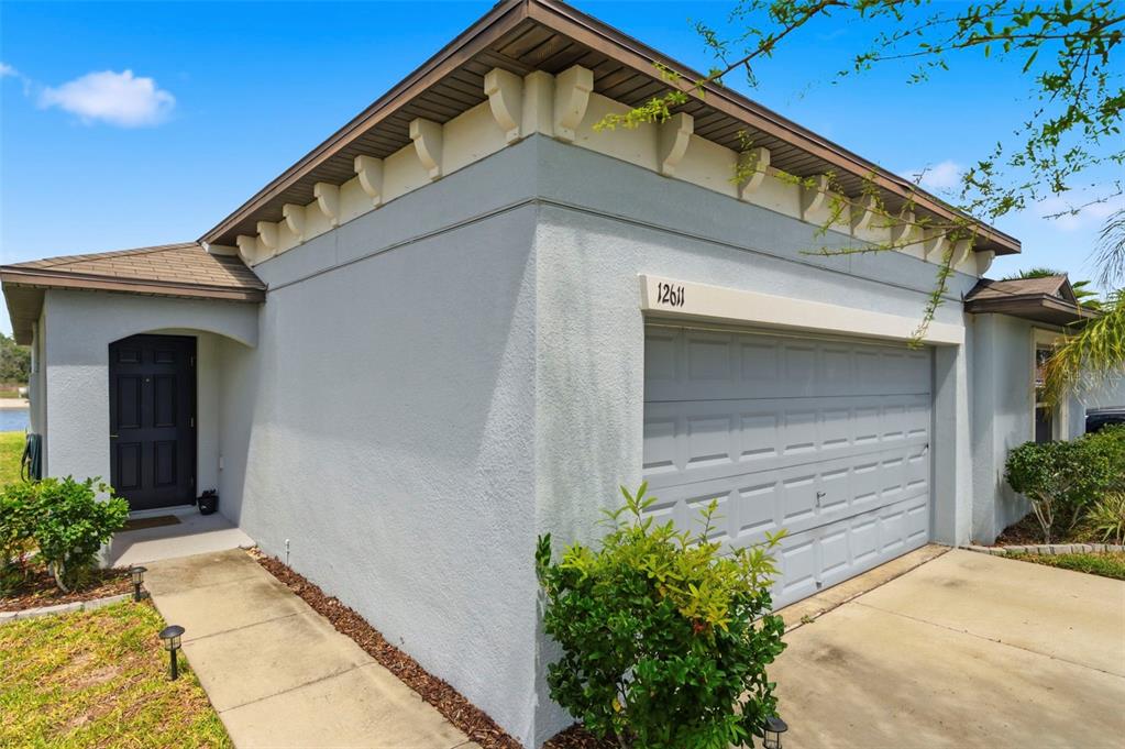 A single-story house exterior features a gray stucco facade, a garage, and a front entrance — 12611 LEMON PEPPER DRIVE, RIVERVIEW, FL