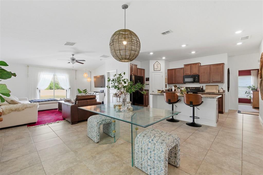 An open-concept living and dining area features tile flooring, a glass table, and kitchen island — 12611 LEMON PEPPER DRIVE, RIVERVIEW, FL