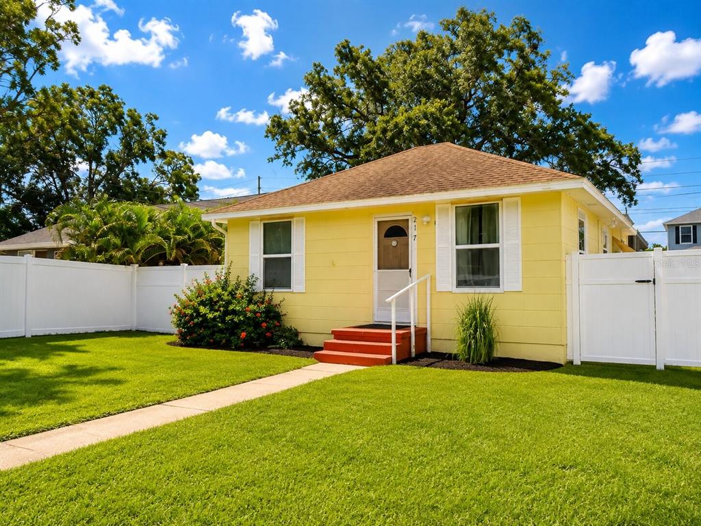 A yellow single-story house with a white fence, a green lawn, and red front steps — 217 50TH TER N, ST PETERSBURG, FL