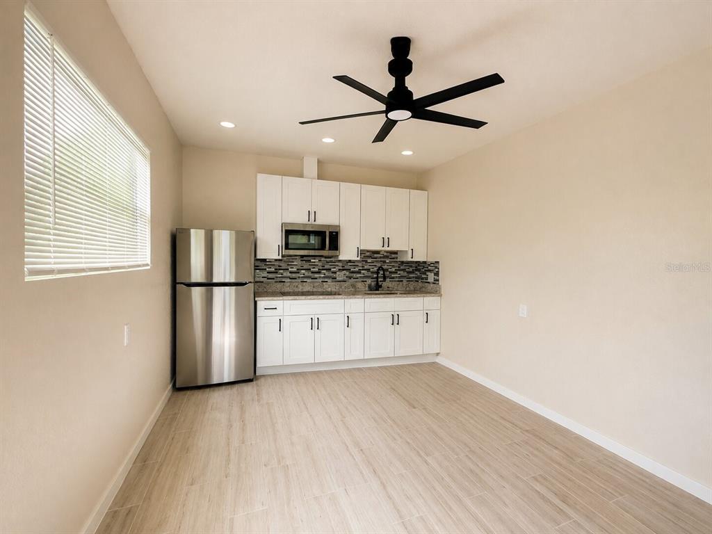 A kitchen features white cabinets, stainless steel appliances, a tiled backsplash, and light wood flooring — 217 50TH TER N, ST PETERSBURG, FL