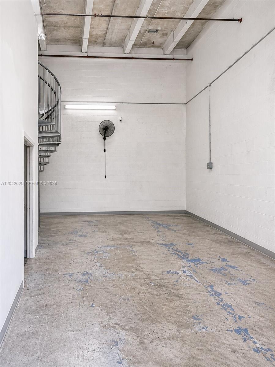 An industrial-style room features a concrete floor, white block walls, and a metal spiral staircase — 6020 NW 99th Ave # 205, Doral FL 33178, DORAL, FL