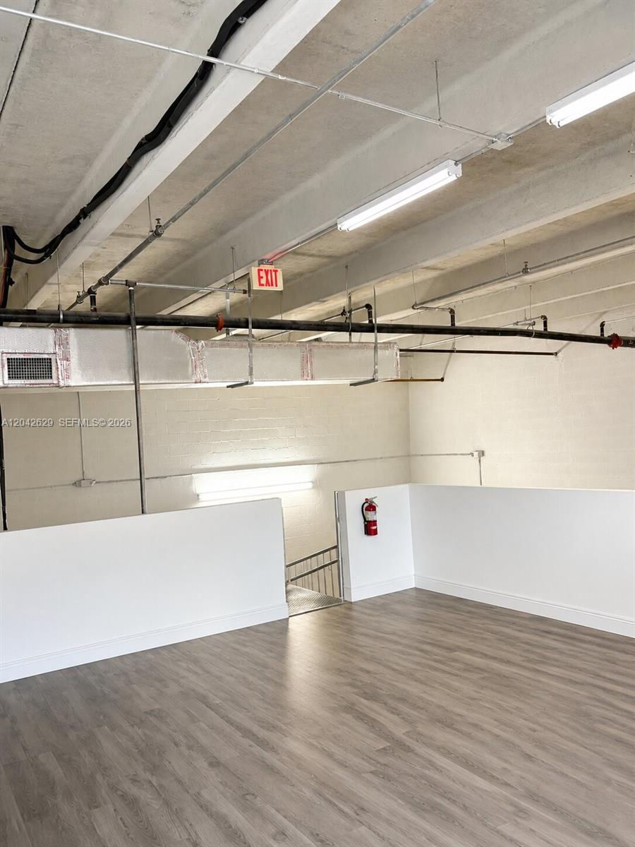 An industrial-style room features exposed ceiling pipes, a white half-wall, and wood-look flooring — 6020 NW 99th Ave # 205, Doral FL 33178, DORAL, FL