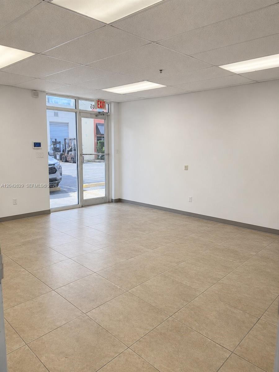 An empty office space features white walls, beige tile flooring, and a glass entry door — 6020 NW 99th Ave # 205, Doral FL 33178, DORAL, FL