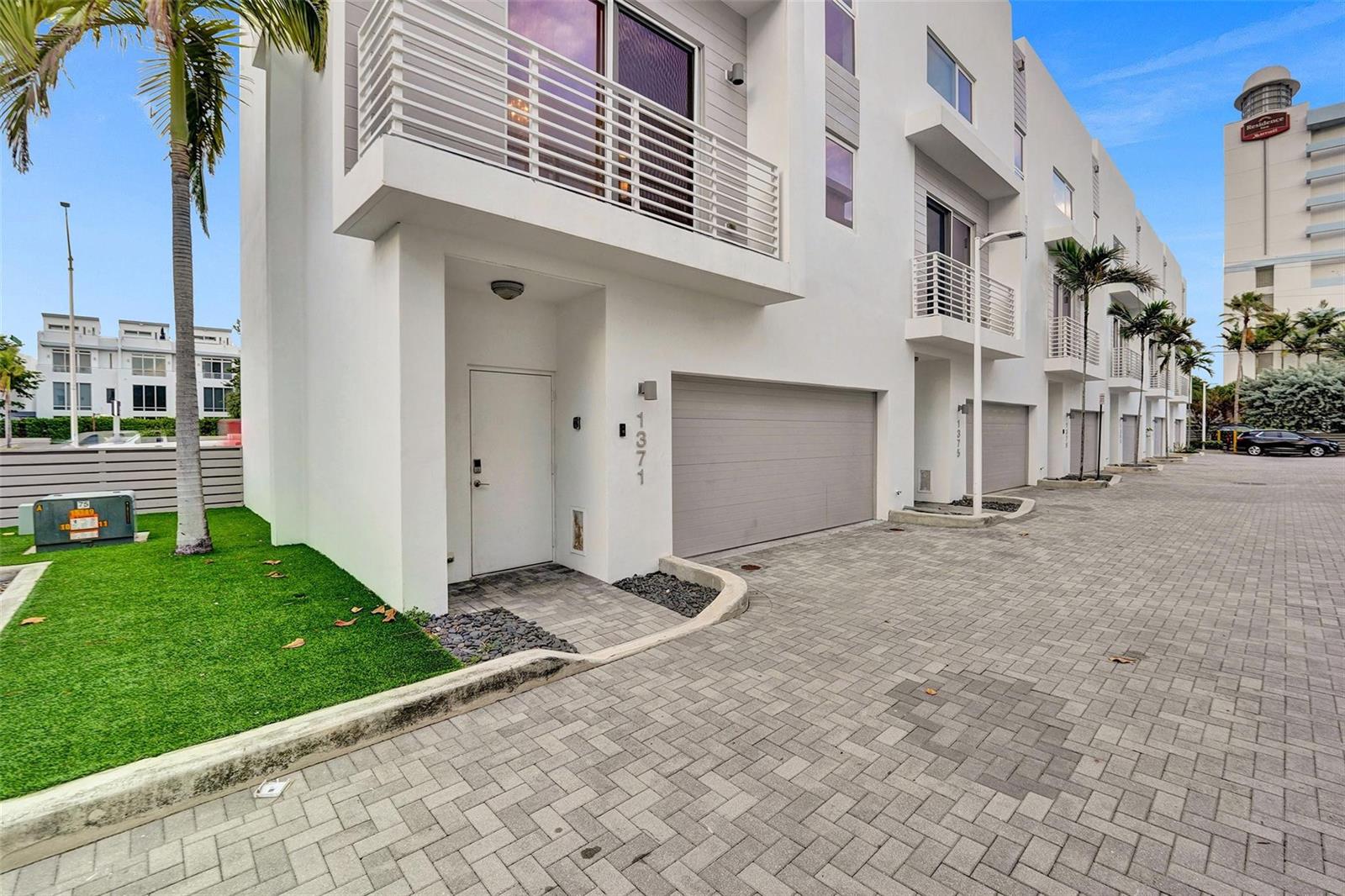 A modern white townhome exterior features a garage, a front door, and a balcony — 1371 N Ocean Boulevard, Pompano Beach FL 33062, POMPANO BEACH, FL