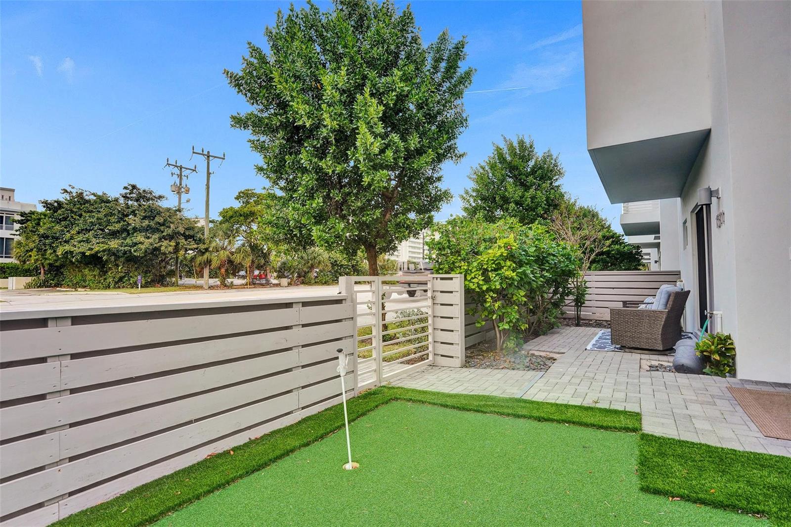 A small backyard features a putting green, a paved patio, and a horizontal wood fence — 1371 N Ocean Boulevard, Pompano Beach FL 33062, POMPANO BEACH, FL